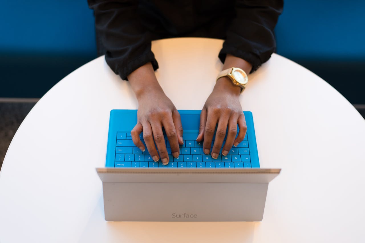 a person wearing a watch and a black sweater types on a blue laptop keyboard